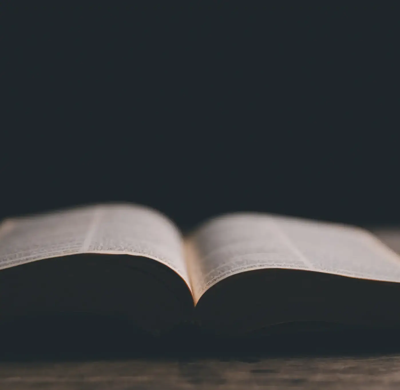An open book resting on a wooden surface against a dark background.