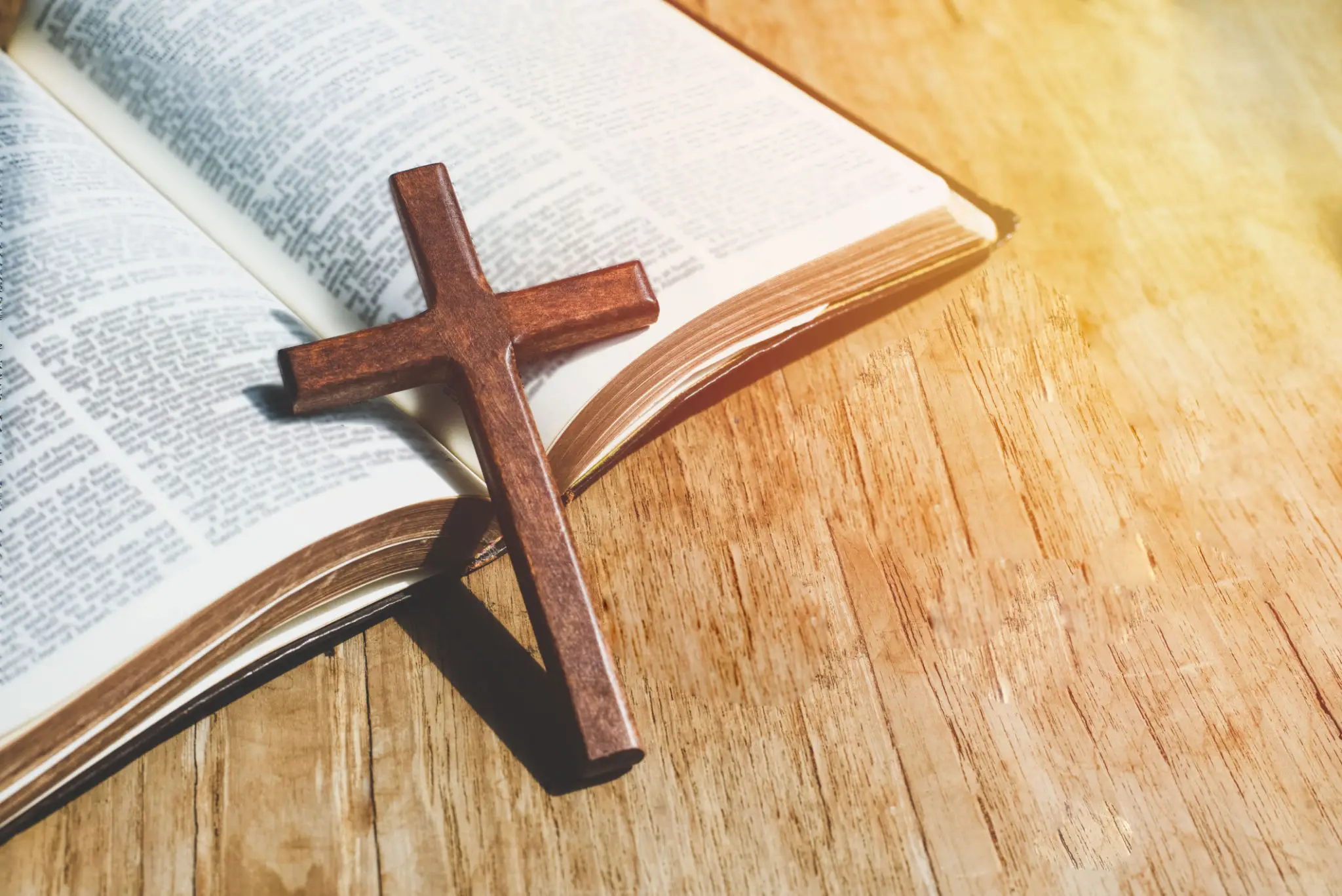 Wooden cross on an open Bible with sunlight.