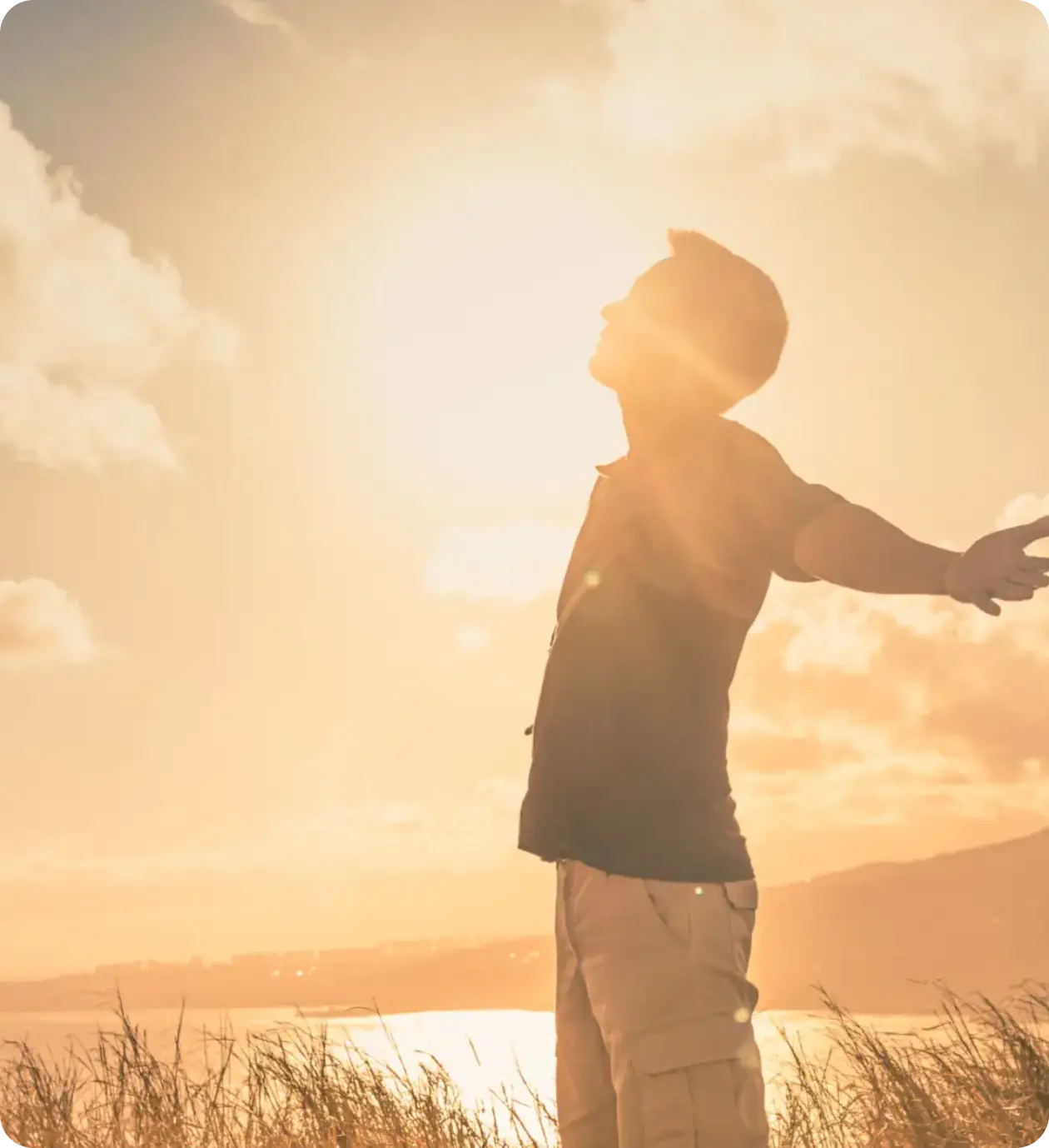 Person embracing sunlight with arms wide open at sunset.